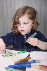 little blonde girl painting with her hands on a paper at home.