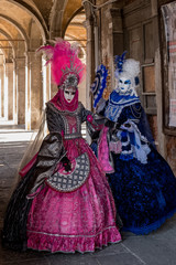 Two women in masks and ornate blue and pink costumes standing near the Rialto Market at Venice Carnival (Carnivale di Venezia)