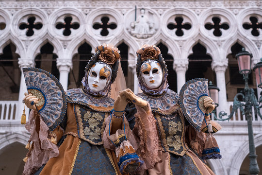 Two women in ornate costumes and painted masks, standing in St Marks Square during Venice Carnival (Carnivale di Venezia)