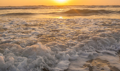 Close-up of waves on a sandy beach at sunset