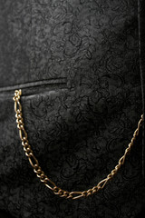 Fototapeta na wymiar goldene Uhrenkette einer Taschenuhr hängt aus einer schwarzen Westentasche