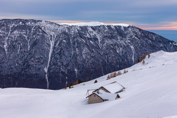 Small mountain farmhouses on snowy slope with, mountain and forest  background, Belluno, Veneto, Italy