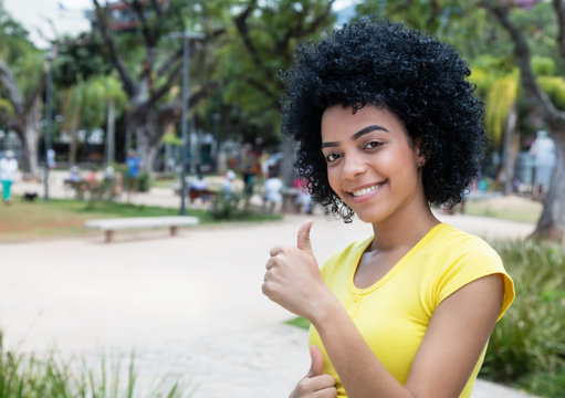 Laughing young adult woman with curly black hair showing thumb up