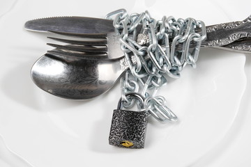 cutlery - spoon, fork and knife wrapped with chain and locked on padlock on white plate, diet concept