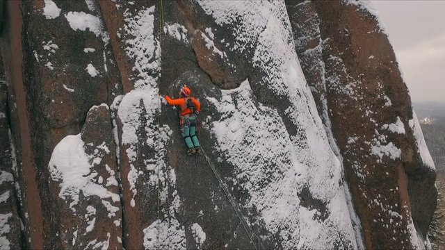 Aerial view of a rock climber climbing a steep cliffs during a sunny winter day.