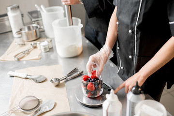 Putting berries into the small jar weighting ingredients for the ice cream production