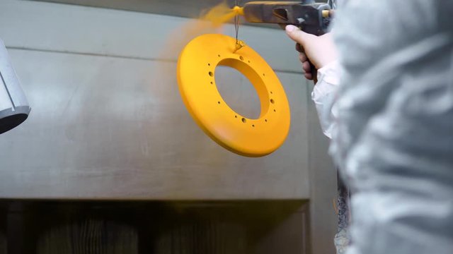 Powder coating of metal parts. A man in a protective suit sprays powder paint from a gun on metal products