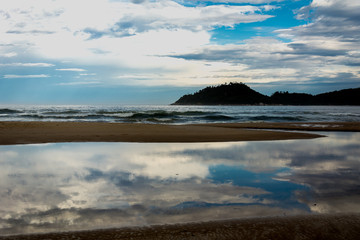 Landscape of the sea with an island at the backside and a puddle with the reflection of the clouds