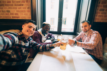 Cheerful old friends having fun taking selfie and drinking draft beer in pub