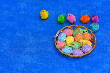 Fototapeta premium Decor of Easter eggs and chickens in a basket on a blue isolated background. The chickens are jumping into the basket.