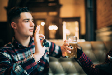Do not drink and drive. Young guy is holding car keys and refusing to drink beer from his friend in...