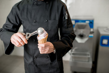 Chef cook filling with white ice cream a waffle cone indoors. Cropped image with no face focused on hands