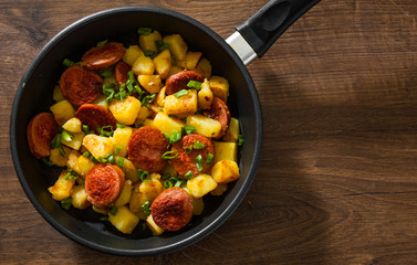Roasted Potato and Sausage in frying pan on wooden table. Top view with copy space