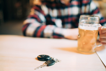 Don't drink and drive concept. Close up of man hand drinking beer near car keys on table. Responsibly and safety driving