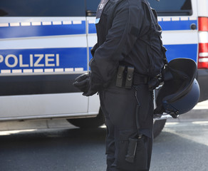Polizist mit Uniform und Helm vor einem Einsatzfahrzeug 