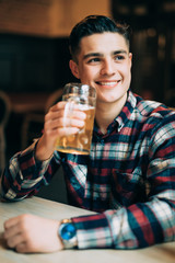 Man in beer pub. Cheerful young man holding a beer mug and smiling while sitting in pub