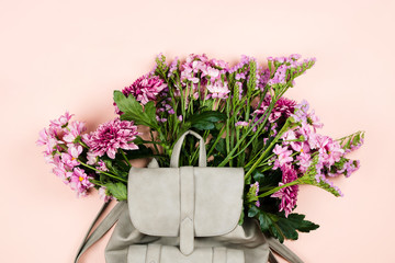 Grey backpack with beautiful flowers bouquet inside. Pastel background, flatlay