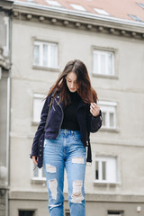 fall outfit fashion details, young stylish woman wearing a suede leather jacket, ripped jeans and black ankle boots. fashion blogger holding a trendy black purse.