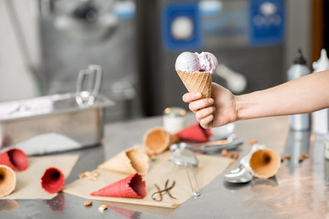 Holding waffle cone with ice cream at the kitchen with food ingredients and ice cream maker machine on the background
