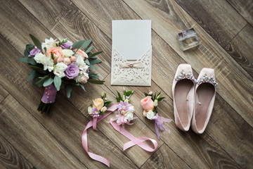 bridal accessories such as shoes, invitation card, rings, perfume, bouquet lie on a wooden background