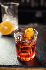 Glass of  whiskey (cognac or brandy) with lemon and ice cubes standing on the bar counter with a bottle on the background