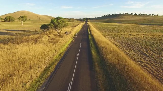 Forward flight rising high above straight rural road among pastures at sunset in Australia