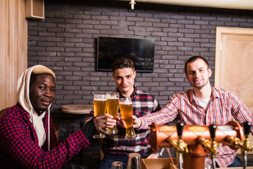 Handsome men's are clinking glasses of beer and smiling while resting in pub