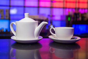 White teapot and tea cup on color lights background
