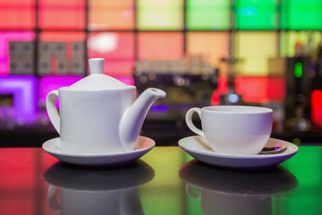 White teapot and tea cup on color lights background
