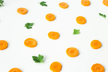 Bright round ringlets of carrots and green twigs of parsley on a white background. Healthy food concept. Top view, flat lay