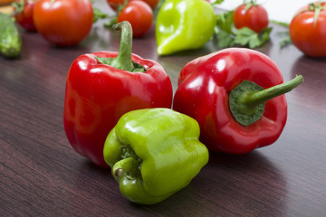 Green and red bell peppers on a background of tomatoes. Two red peppers on a cinnamon wooden background