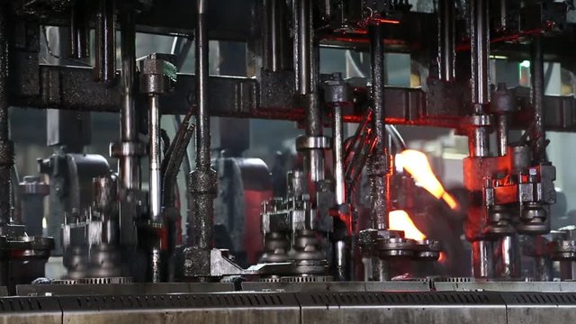 Hot glass is fed from the oven to the glass bottle making machine. Machine in the glass factory produces glass bottles Automated Production Line of Bottle In Factory. Ambient sound at factory.