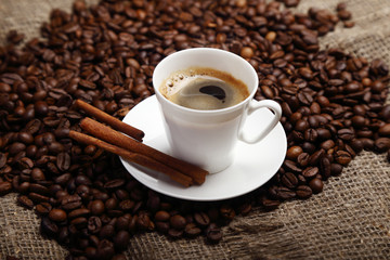 Coffee beans, white cup and saucer, cinnamon sticks.