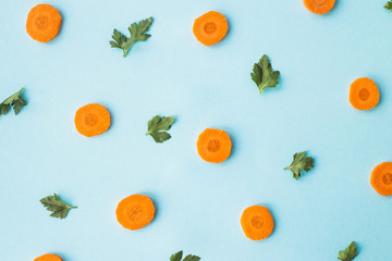 Bright round ringlets of carrots with green parsley sprigs on a blue background. Top view, flat lay