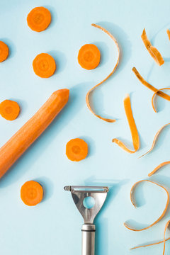 Carrot cleaning with a special kitchen appliance. On a blue background. Bright carrot shavings and rings. Top view, flat lay