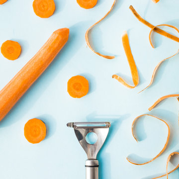 Carrot cleaning with a special kitchen appliance. On a blue background. Bright carrot shavings and rings. Top view, flat lay