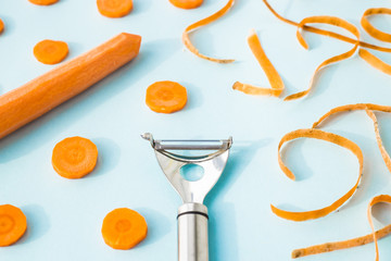 Carrot cleaning with a special kitchen appliance. On a blue background. Bright carrot shavings and rings. Top view, flat lay