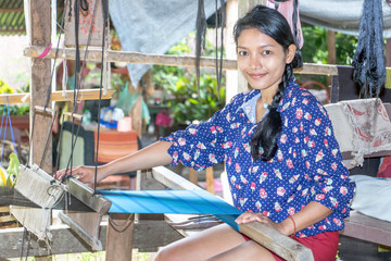 young woman working at home on a weaving loom, Laos countryside.