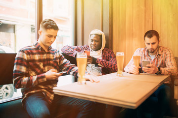 people, men, leisure, friendship and technology concept - Young men multiracial friends with smartphones drinking beer at bar or pub