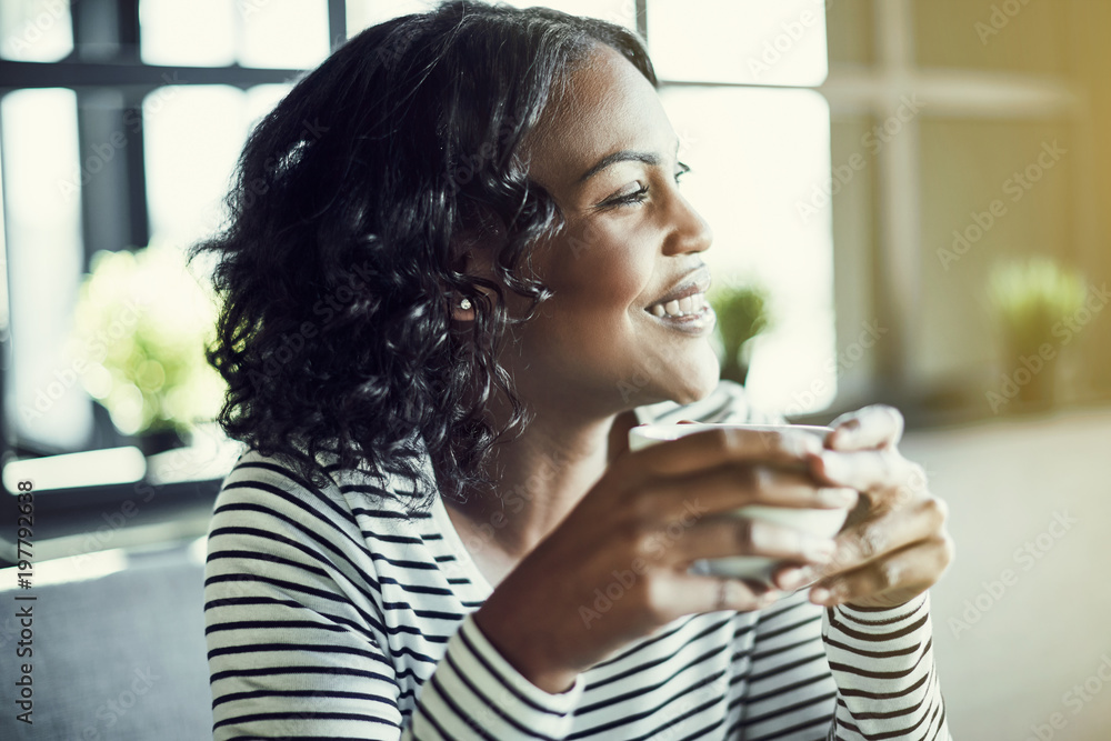 Wall mural Smiling African woman drinking coffee and looking through a wind