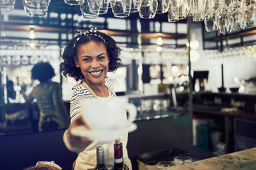 Young barista smiling and holding a cup of coffee