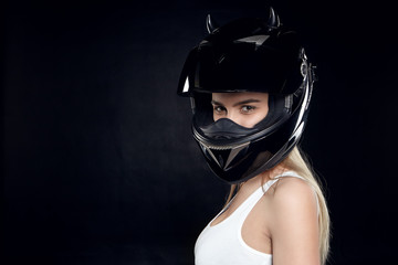 Beautiful self determined young European woman motorcyclist wearing white tank top and protective black helmet posing at blank studio wall with copy space for your text or promotional information