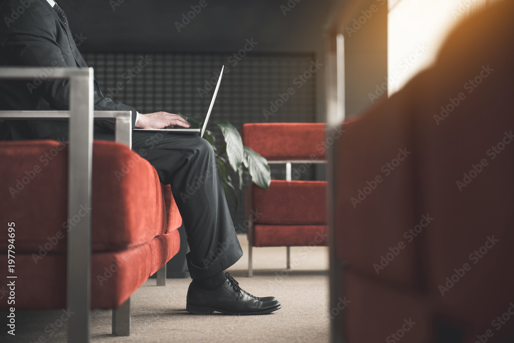 Poster side view profile of male in suit sitting on sofa with computer on his lap and typing. copy space in