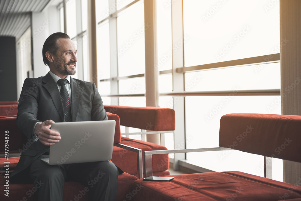 Poster jolly solid man sitting on lounge with notebook, he is looking at window and laughing. copy space in