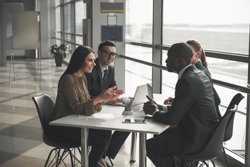 Group of young people in formalwear sitting at office table and talking