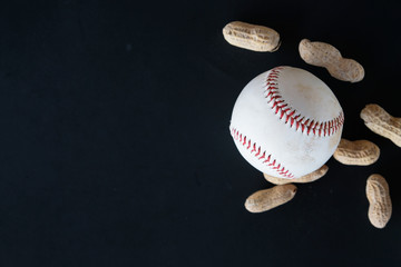 Baseball ball and peanuts as flat lay on black background.  American sports game equipment with athletic feel.