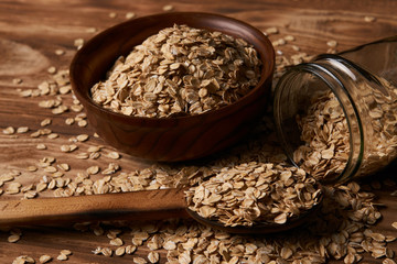 Oat flakes oatmeal in bowl and wooden spoon on wood table background. Healthy vegetarian diet food and agriculture concept