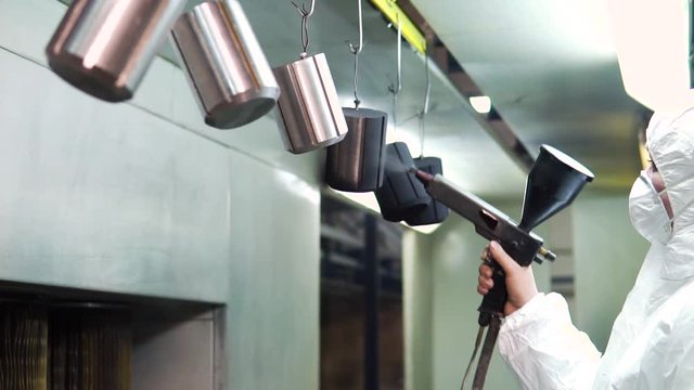 Powder coating of metal parts. A man in a protective suit sprays powder paint from a gun on metal products