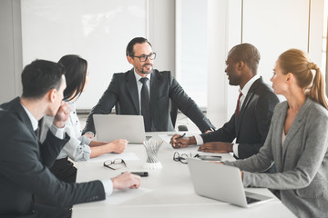 Employees sitting at table in the office and listening to their boss talking