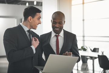 Waist up of satisfied executives standing in the office with laptop in hand and communicating